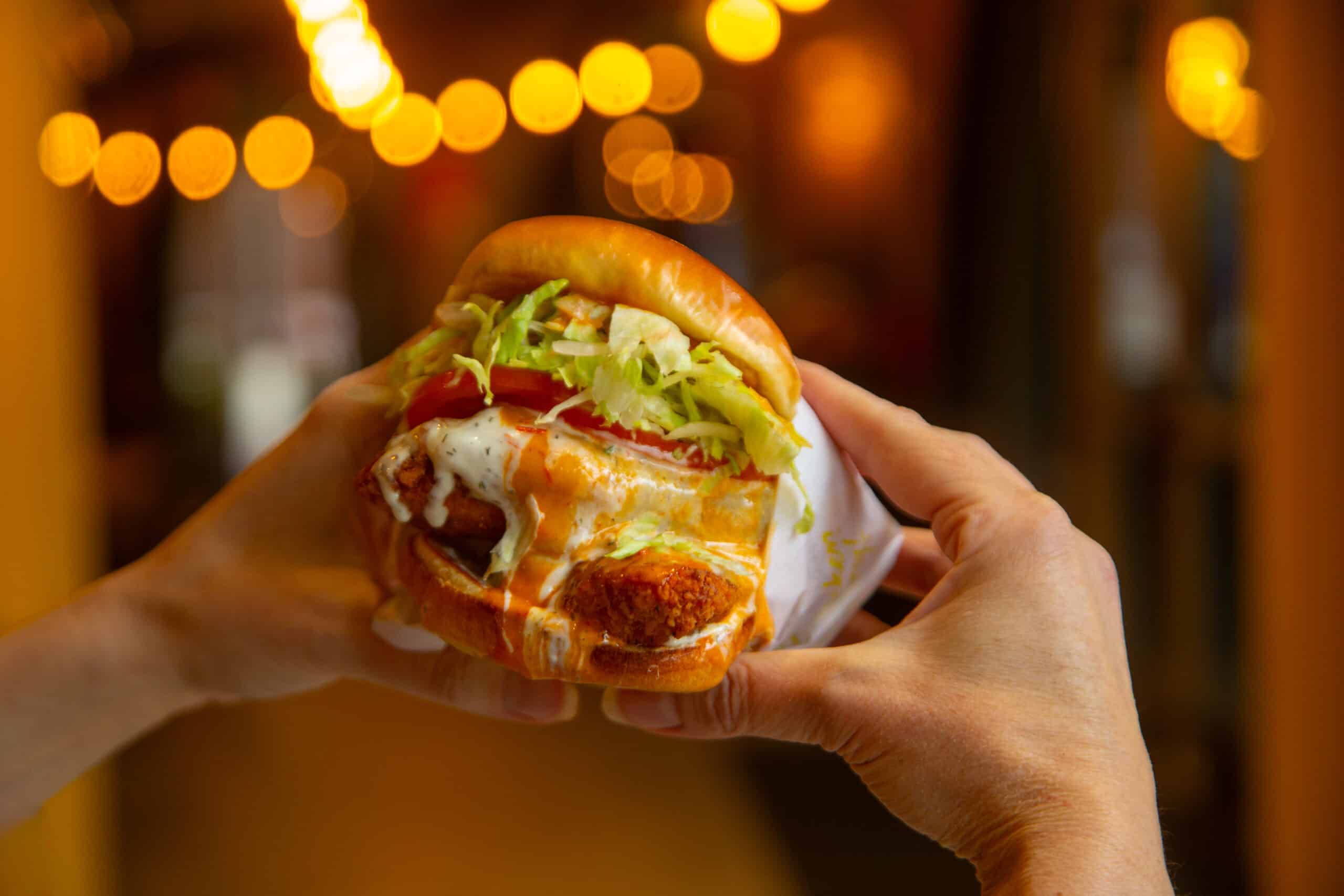 Two hands holding a Calabrian Chicken Sandwich from Chicken Guy!